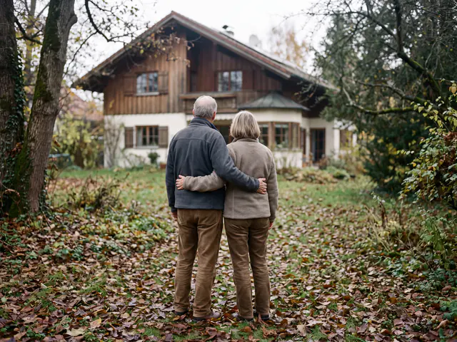 Älteres Paar steht Arm in Arm im herbstlichen Garten und blickt auf sein Haus
